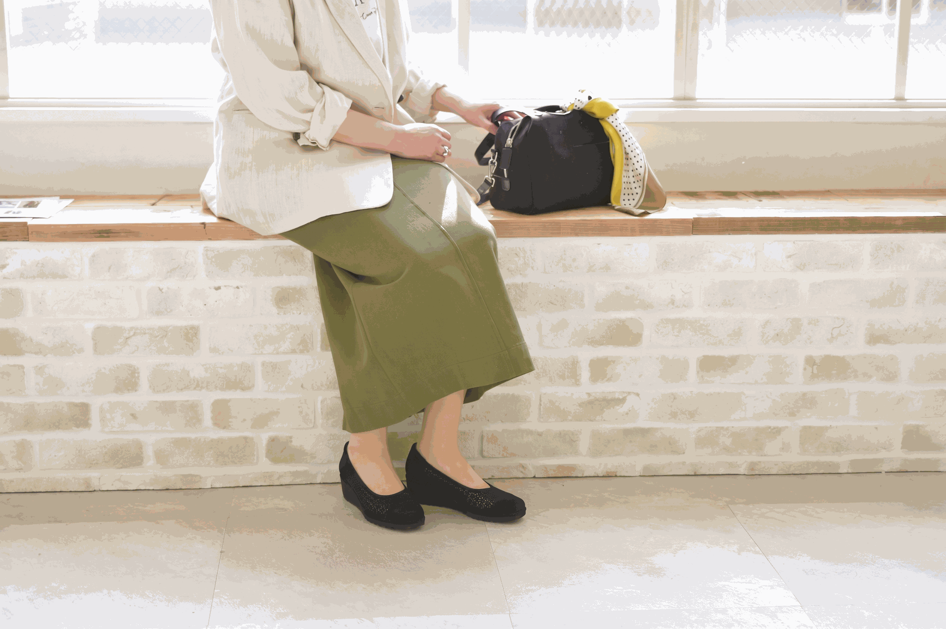 窓辺でシルバーのサンダルを履いてくつろぐ女性の足元